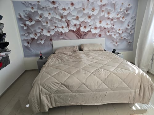 Piumino Wove color sabbia su un letto grande in una camera degli ospiti con carta da parati a fiori