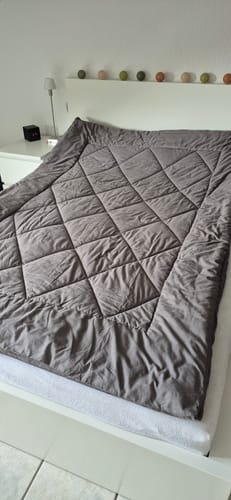 Piumino Wove grigio-beige ripiegato su un letto bianco con lucine sopra