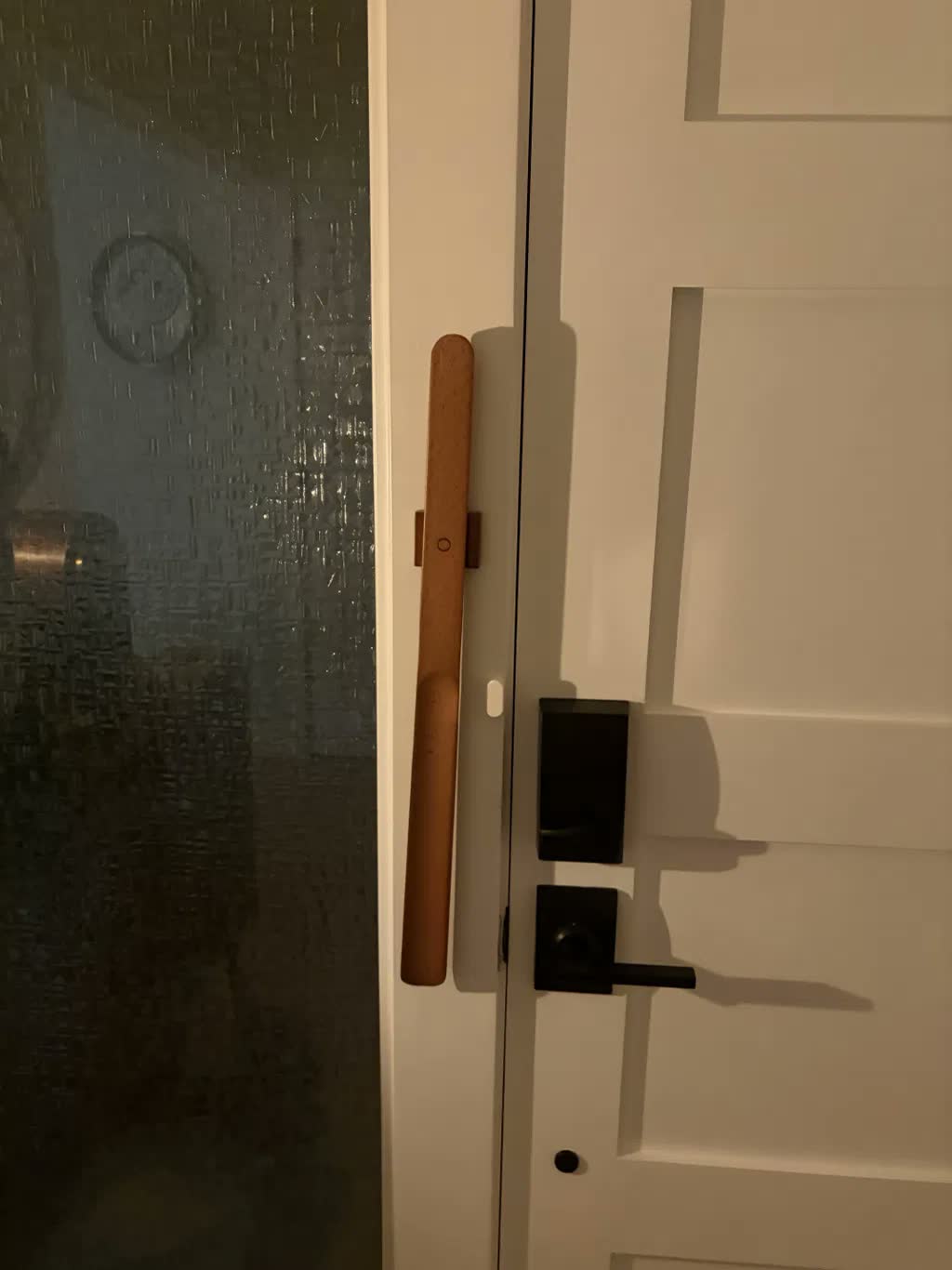 Calzascarpe in faggio chiaro fissato con calamita su uno stipite bianco, accanto a una maniglia nera e a una serratura smart