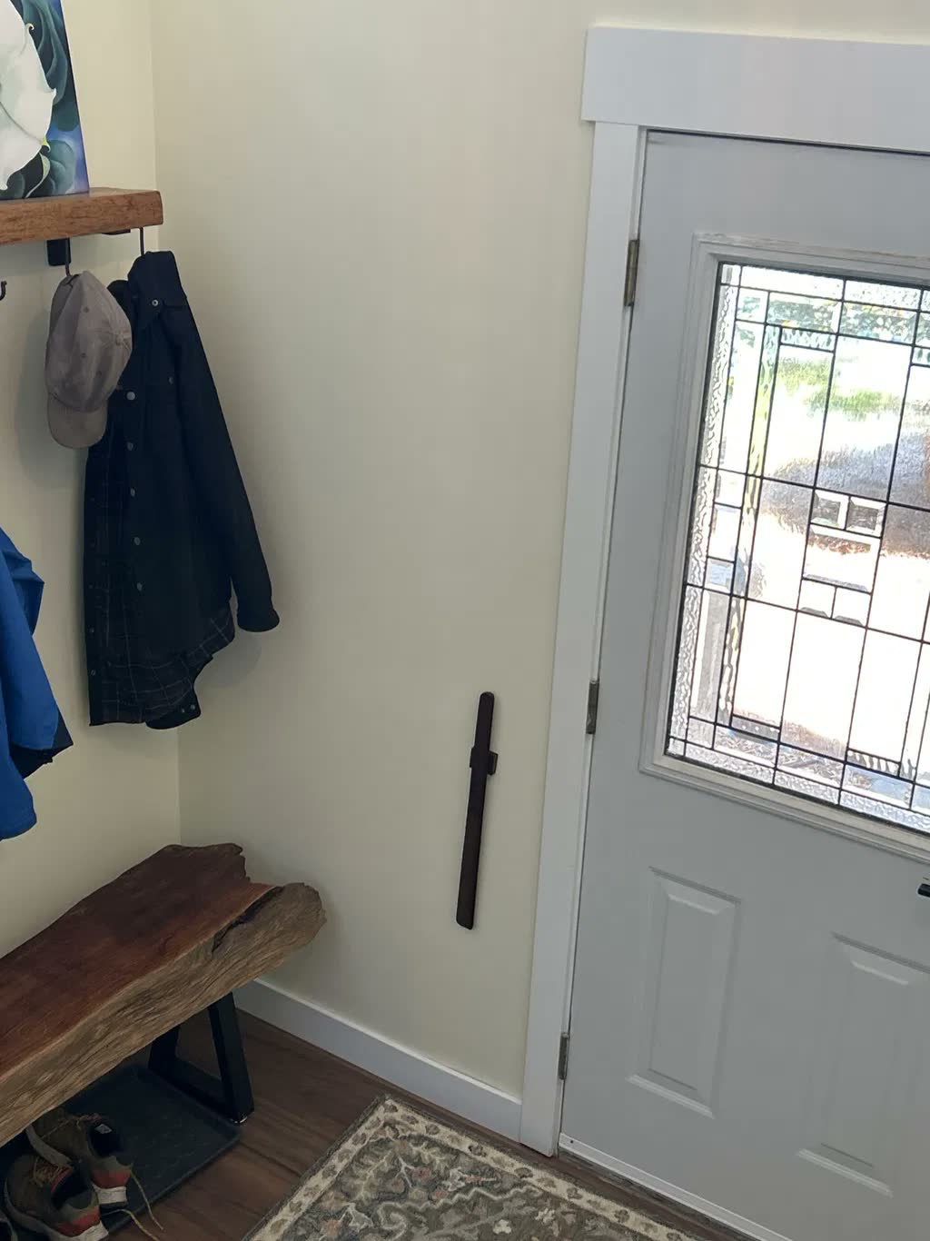 Calzascarpe in noce scuro su una parete crema dell'ingresso con una panca a bordo vivo, appendiabiti e una porta d'ingresso con vetro piombato
