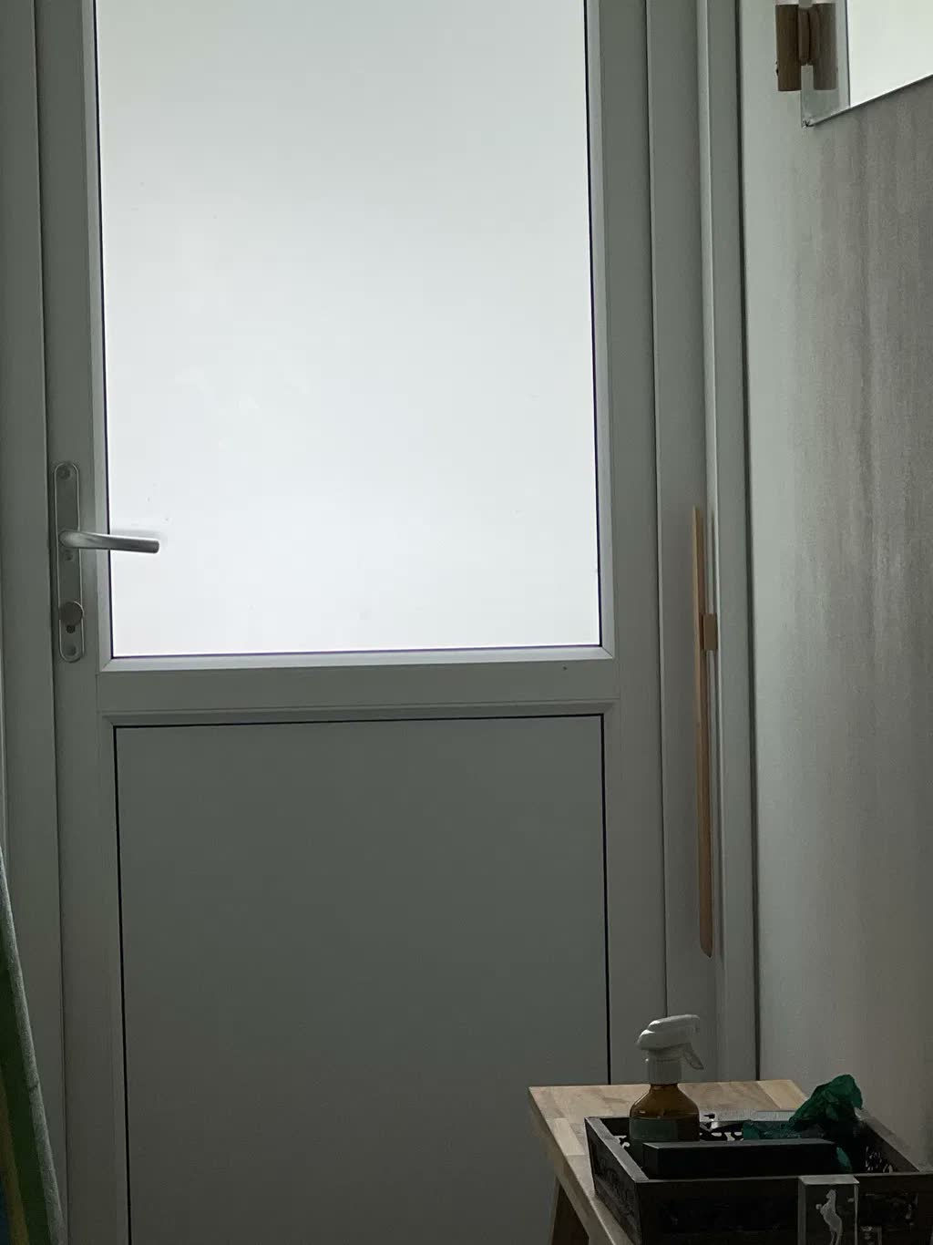 Calzascarpe in faggio naturale su una parete greige accanto a una porta bianca del giardino con vetro satinato
