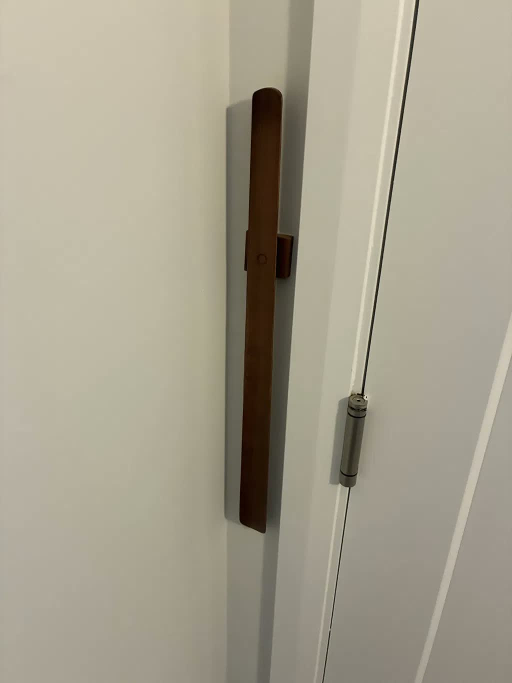 Primo piano di un calzascarpe in noce scuro su una parete bianca accanto a una porta bianca con la cerniera in vista